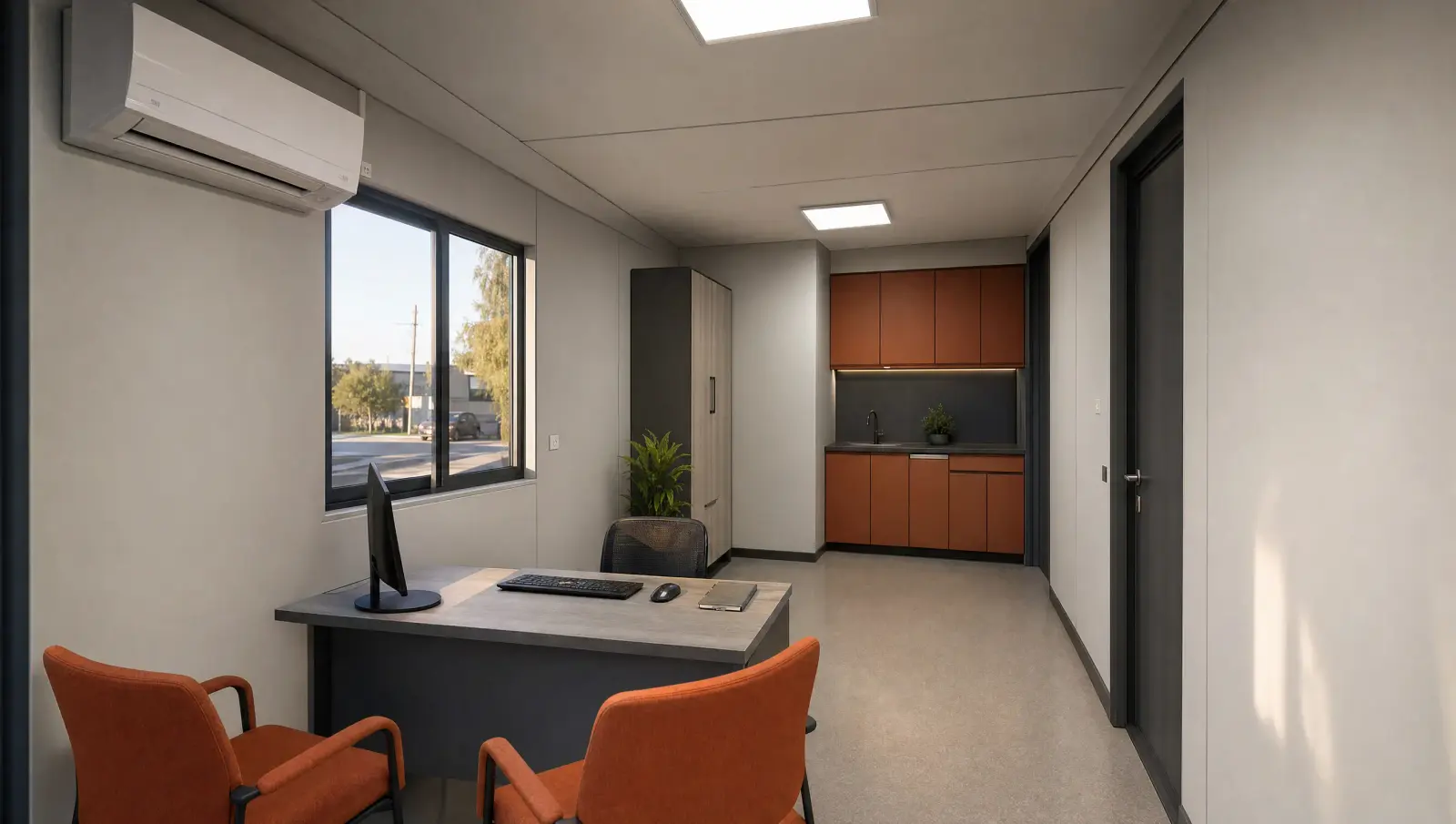 Interior de una oficina modular con escritorio, aire acondicionado, ventana y kitchenette al fondo.